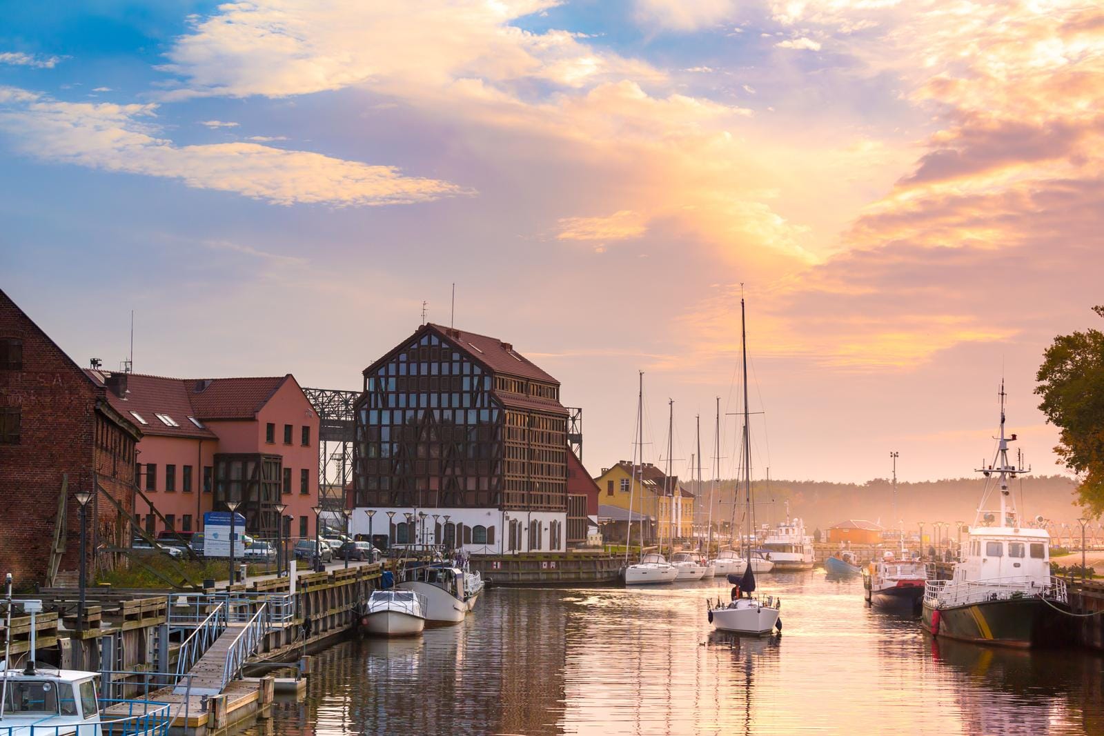 Hafen mit Segelbooten bei Sonnenuntergang, historische Gebäude im Hintergrund.
