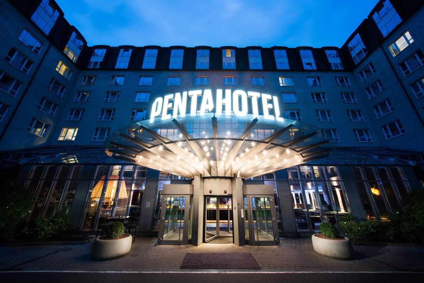 Hotel-Eingang bei Nacht mit beleuchtetem Pentahotel-Logo und moderner GlasĂĽberdachung.