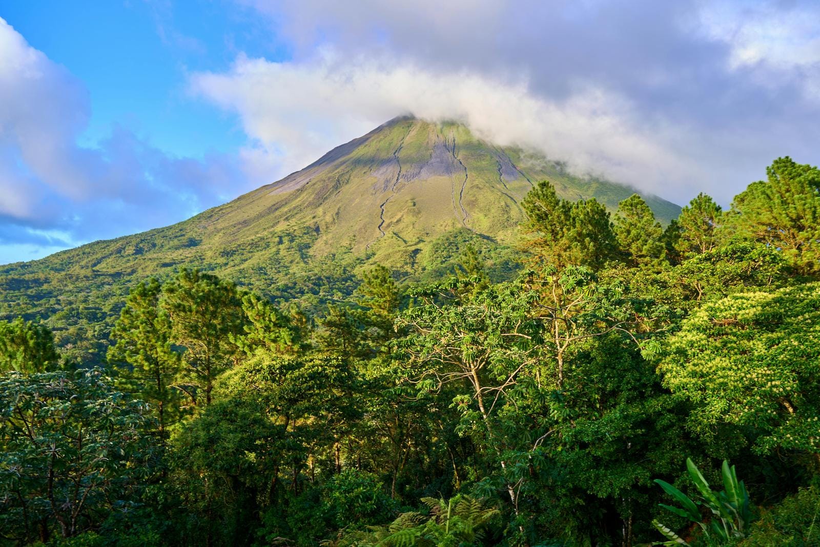 Grüne Vulkanlandschaft in Costa Rica unter blauem Himmel mit Wolken.