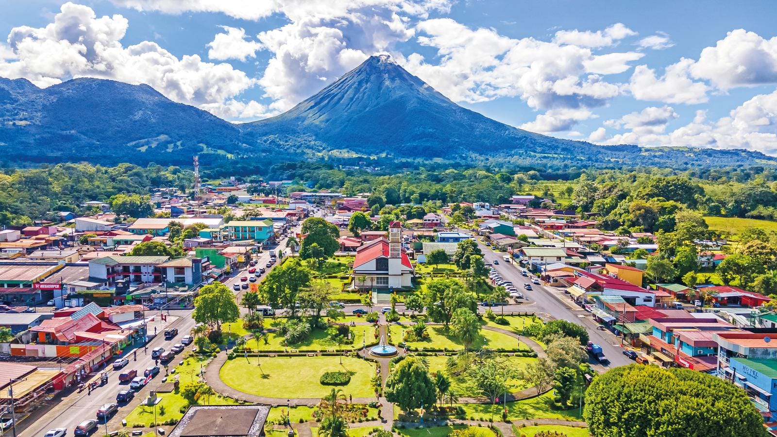 Kleinstadt in Costa Rica mit Vulkan Arenal im Hintergrund, grüne Parkanlage zentral.