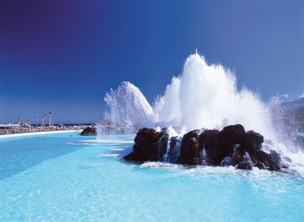 Blaue Lagune auf Teneriffa mit spritzendem Wasser und Palmen, sonnige Entspannung.