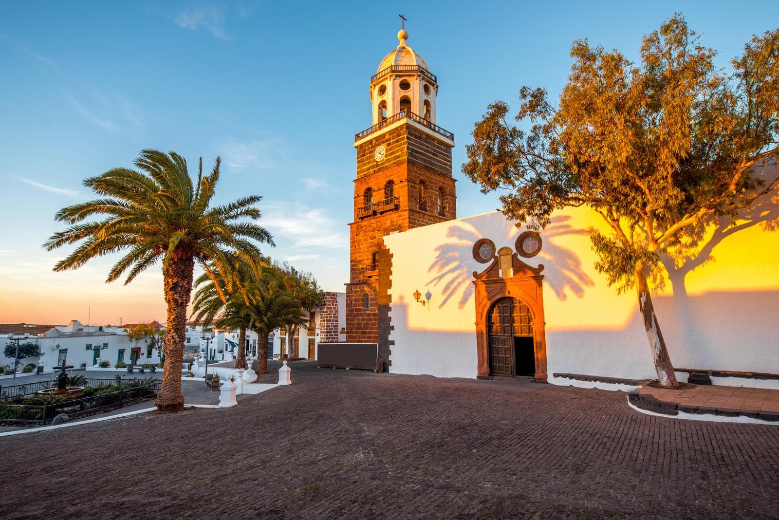 Kirche in Teguise, Lanzarote, im Abendlicht mit Palmen im Vordergrund.