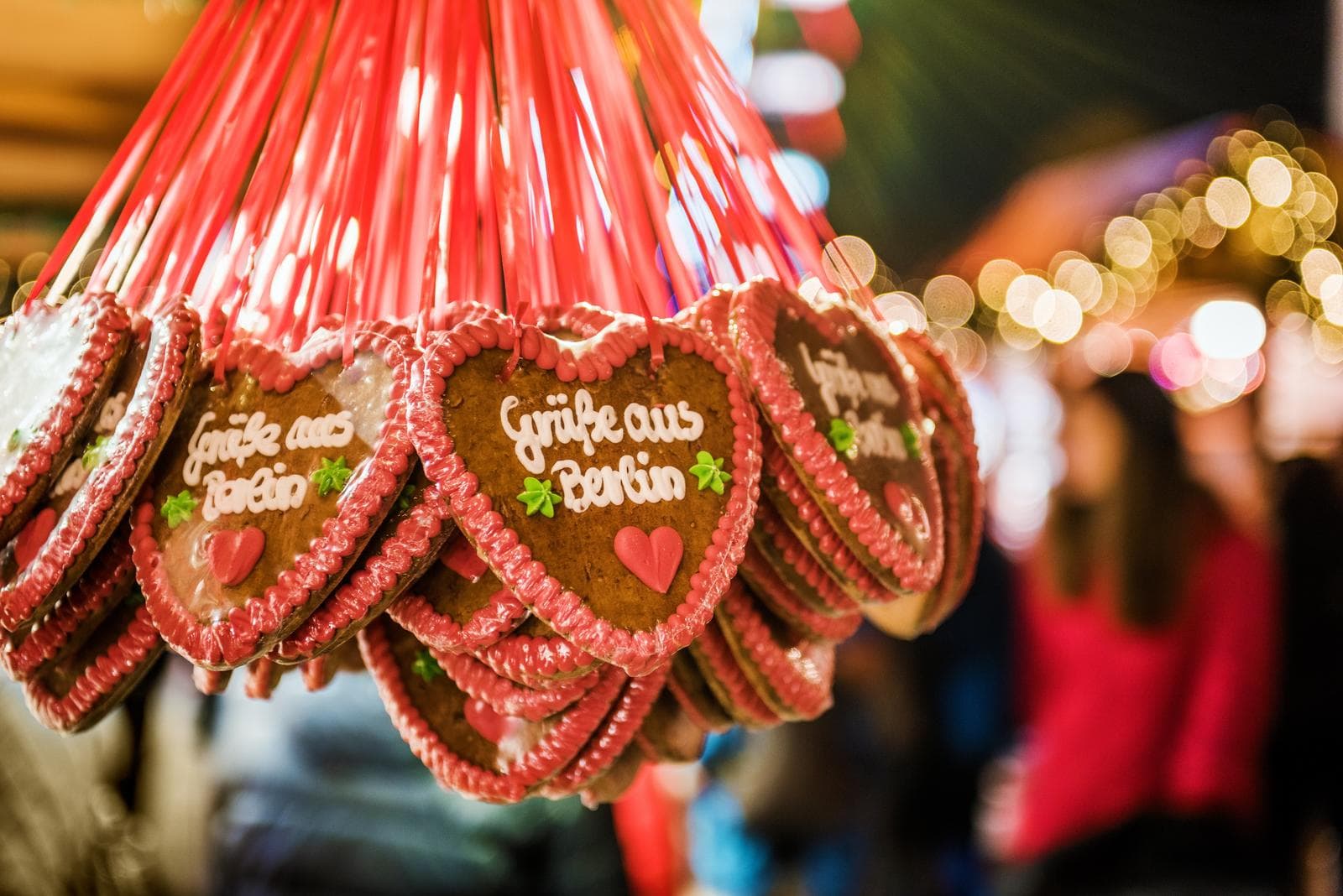 Lebkuchenherzen mit "GrĂŒĂe aus Berlin" auf einem festlichen, bunten Weihnachtsmarkt.