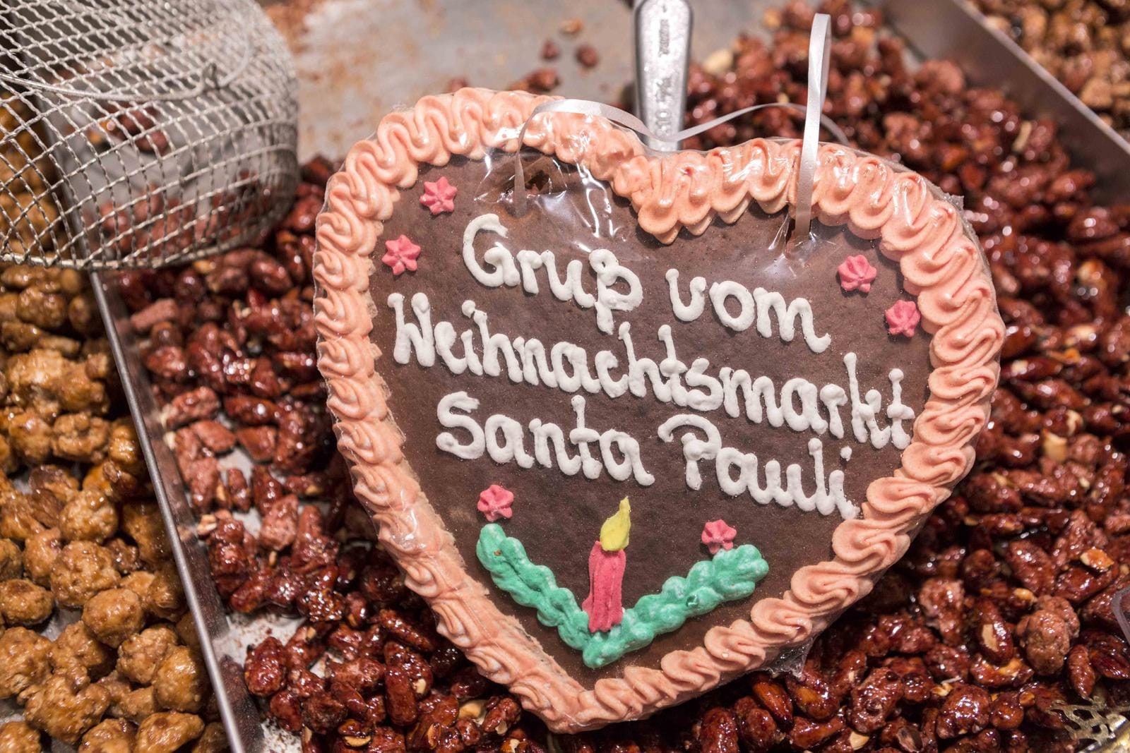 Lebkuchenherz mit rosa Rand auf gebrannten Mandeln, Weihnachtsmarkt-Stimmung.
