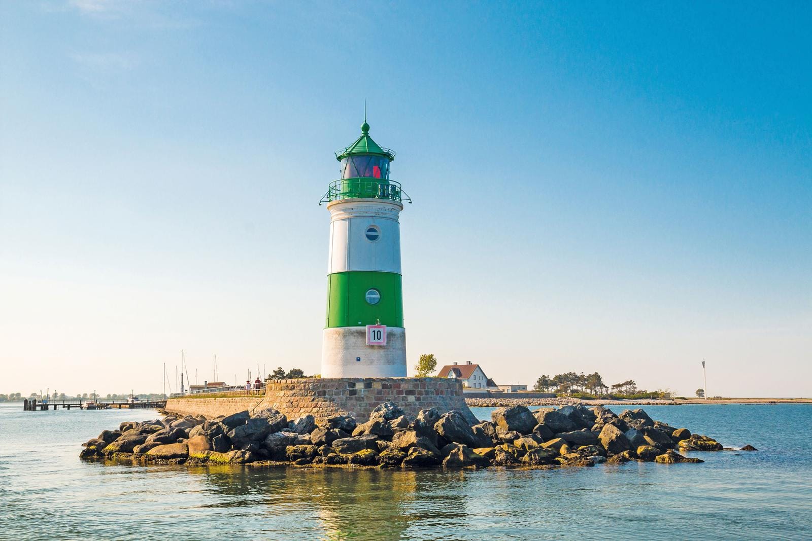 Leuchtturm am Meer in Warnemünde, Deutschland, mit blauem Himmel und ruhiger Küstenlandschaft.