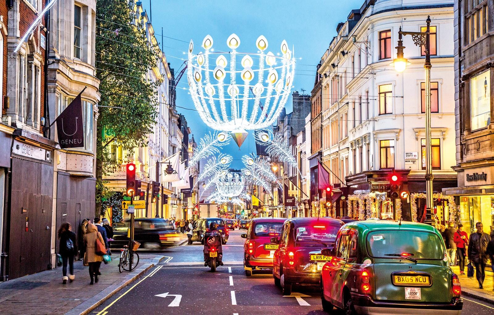 Weihnachtlich beleuchtete Oxford Street in London bei Dämmerung mit Taxis und Fußgängern.