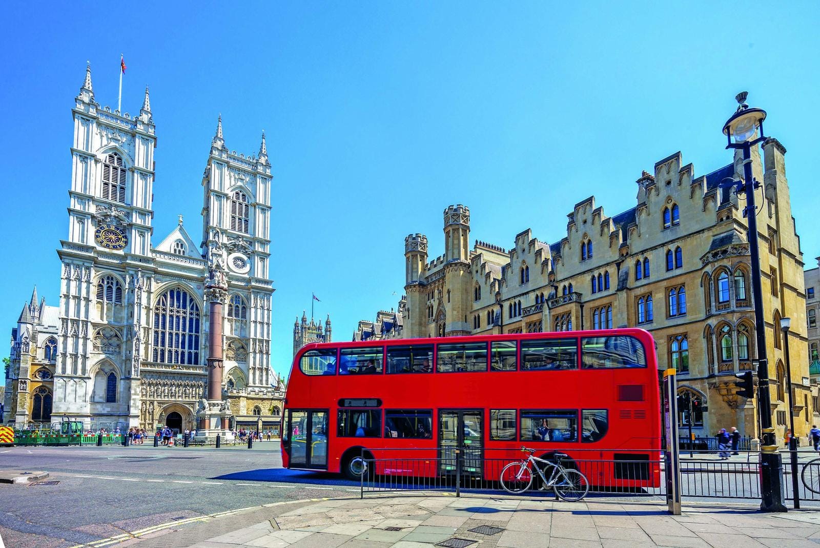 Roter Doppeldeckerbus vor historischer Architektur in London, klarer Himmel im Hintergrund.