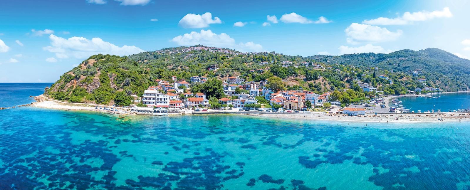 Küstenstadt mit Stränden, türkisfarbenem Wasser, weißen Häusern und grünen Hügeln.