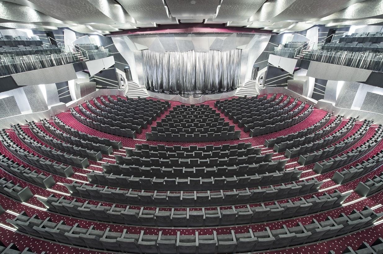 Modernes Auditorium mit grauen Sitzen, rotem Teppich und silbernem Vorhang.