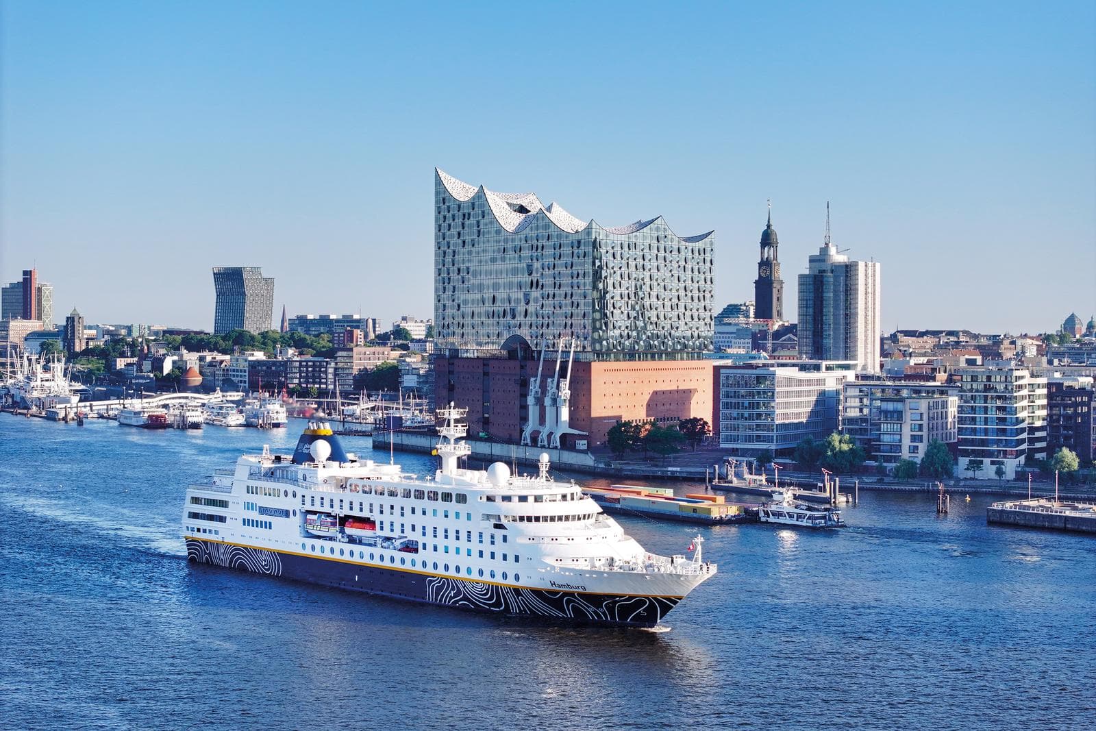 Kreuzfahrtschiff vor der Elbphilharmonie in Hamburg, bei klarem Himmel und Hafenblick.