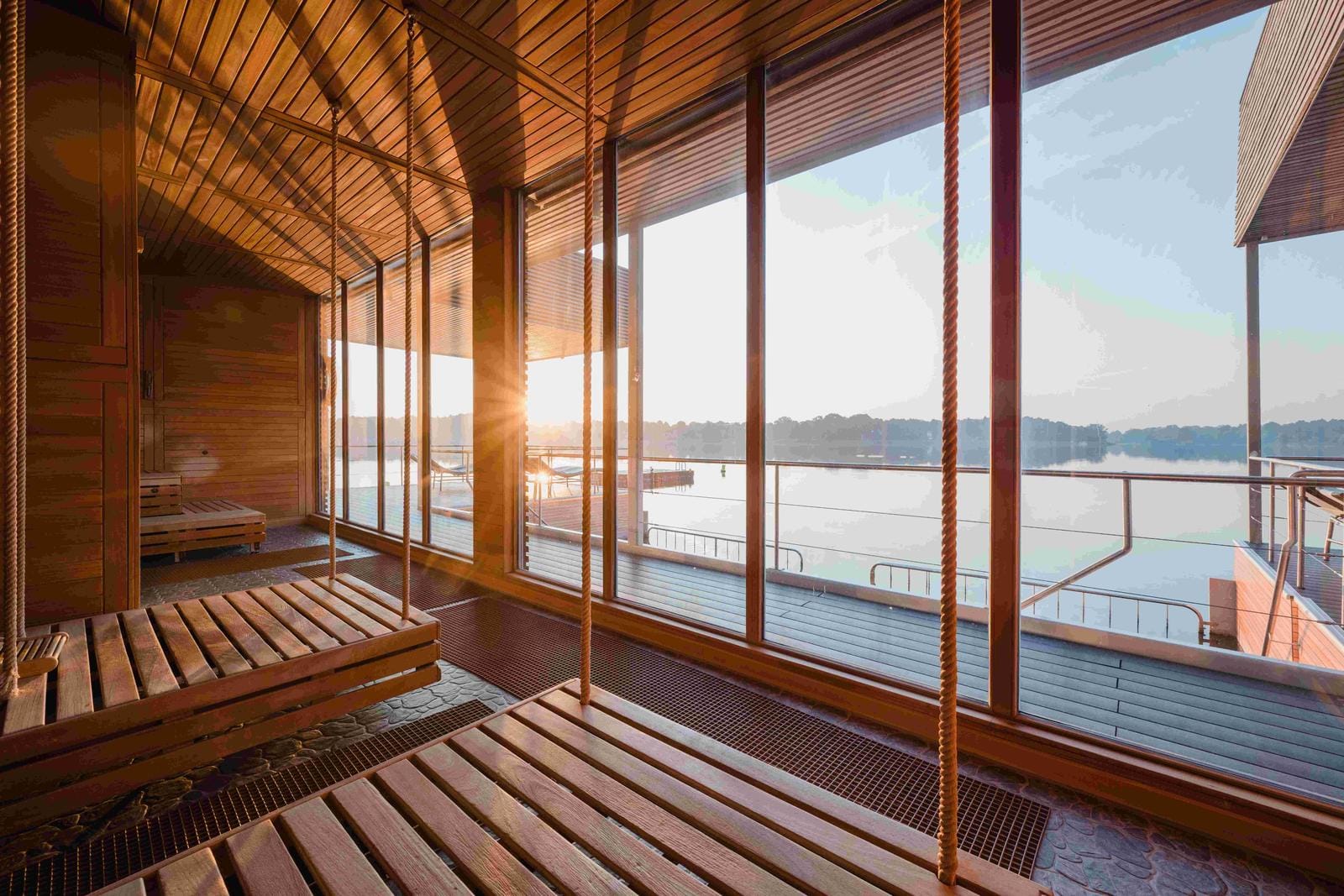 Moderne Sauna mit Holzbänken, großen Fenstern und Seeblick bei Sonnenaufgang.
