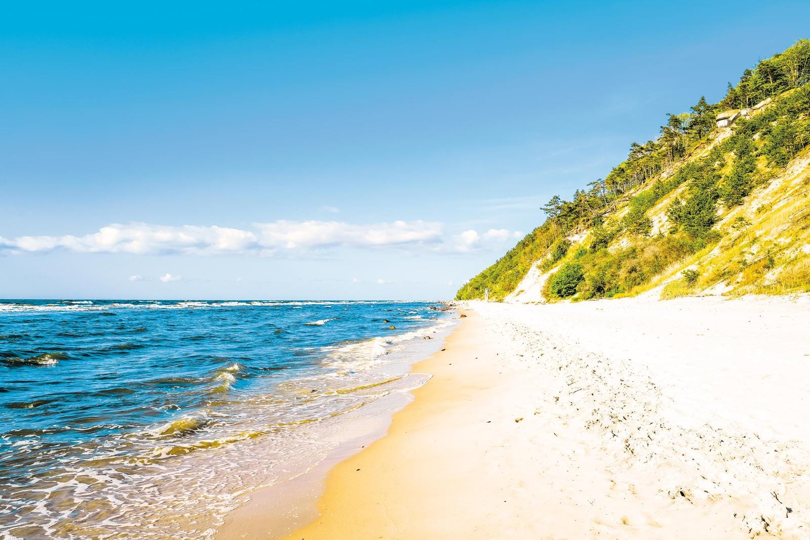Nehrung mit goldenem Sandstrand und blauem Meer unter klarem Himmel.