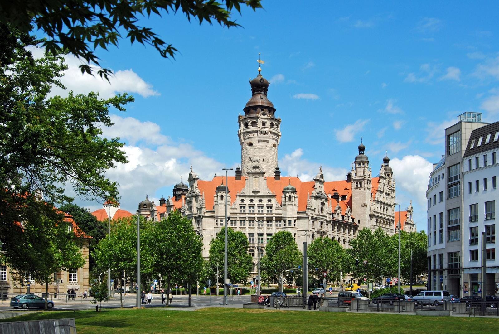 Neues Rathaus, Leipzig, Deutschland; historisch, rotes Dach, blauer Himmel, grüne Bäume.