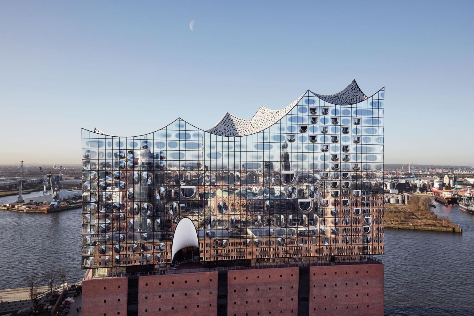 Gläserne Elbphilharmonie über Hafen in Hamburg, modernes Stadtbild mit blauem Himmel.