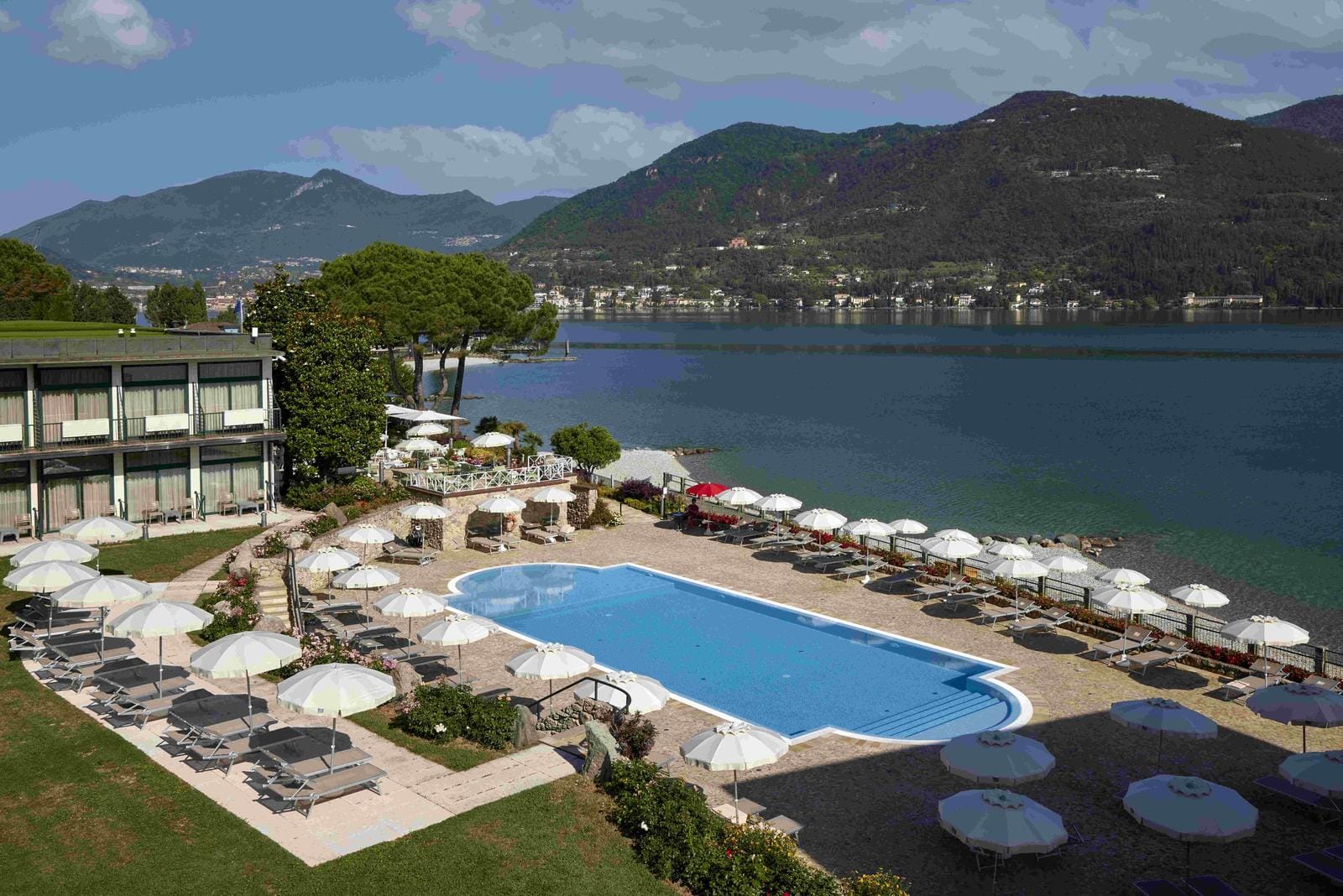 Pool mit Sonnenschirmen, Seeblick, umgeben von grünen Hügeln und blühenden Gärten.