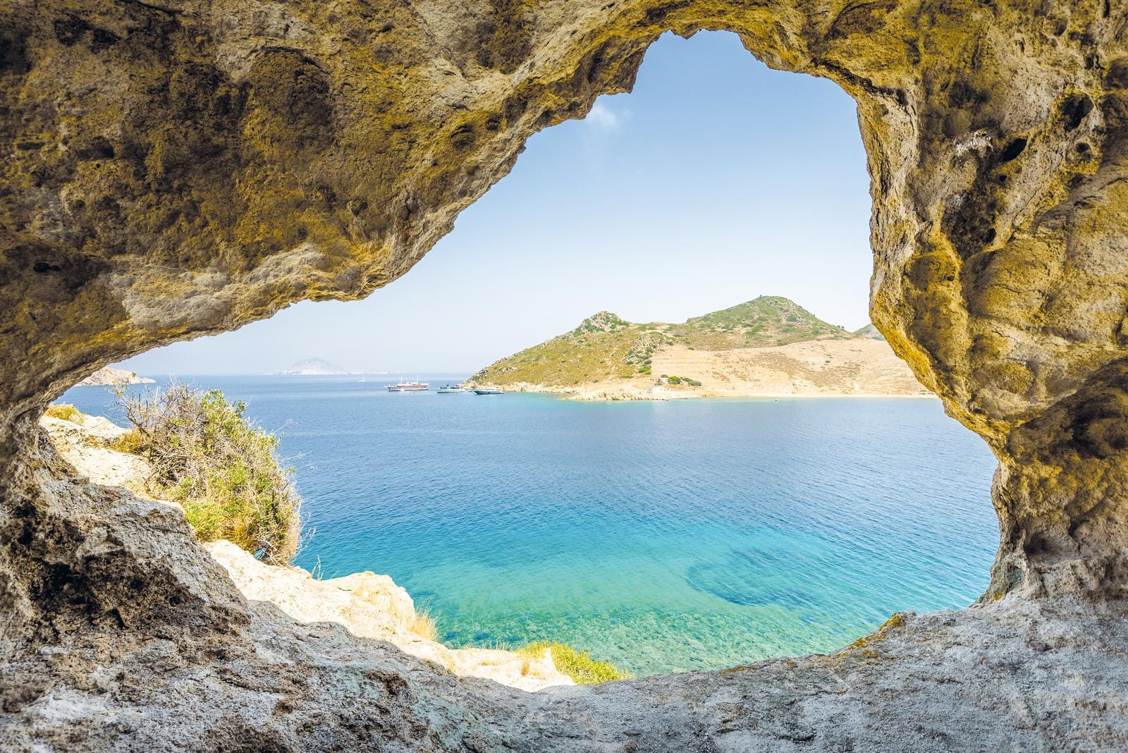 Blick durch eine Höhlenöffnung auf türkises Meer und felsige Insel mit klarem Himmel.