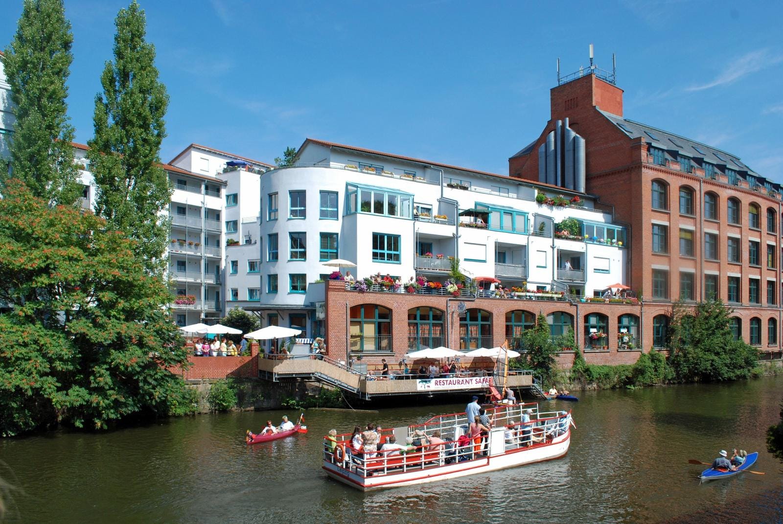 Haus am Wasser mit roten Ziegeln, weiĂźen Fassaden und Booten auf dem Fluss.
