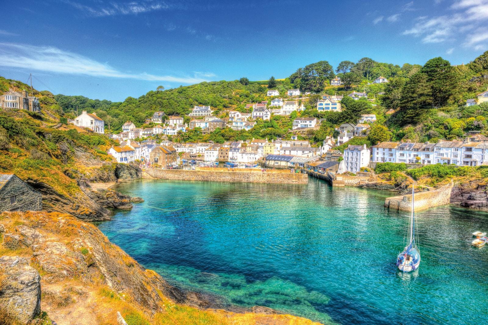 Malerisches Küstendorf in Cornwall mit blauem Wasser und weißen Häusern auf grünen Hügeln.