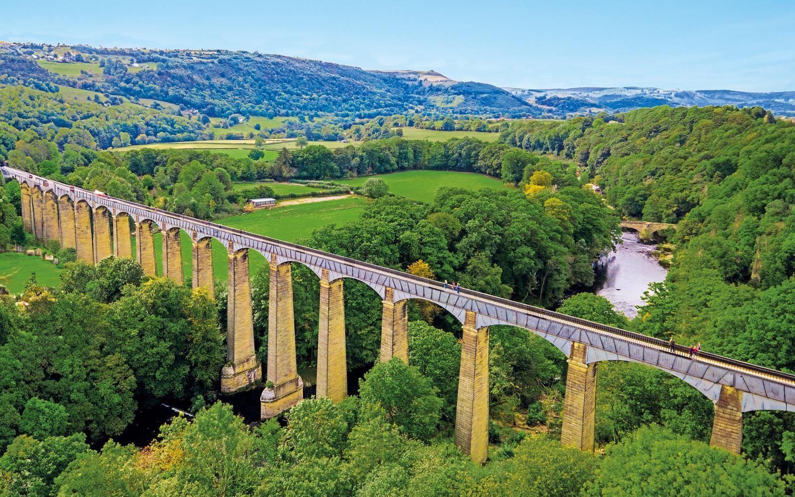 Langes Viadukt in grüner Landschaft von Wales mit Fluss und bewaldeten Hügeln.
