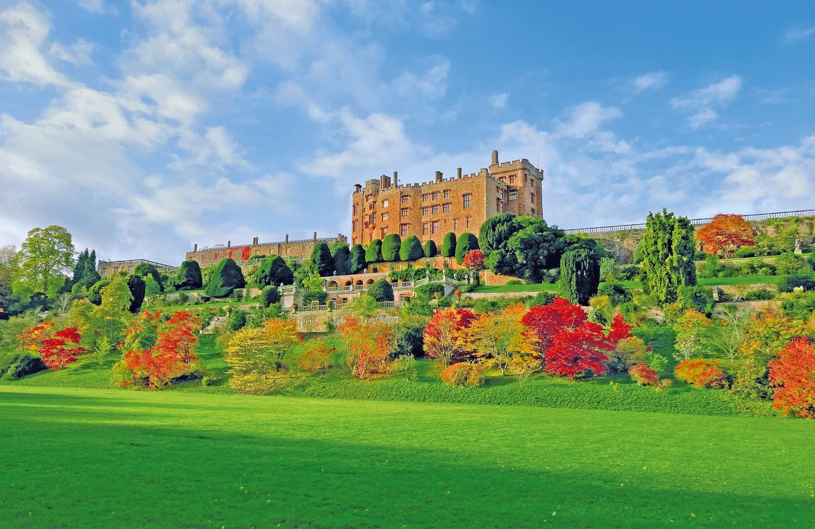 Impressionantes Schloss auf grünem Hügel mit farbenfrohen Bäumen im Herbst.
