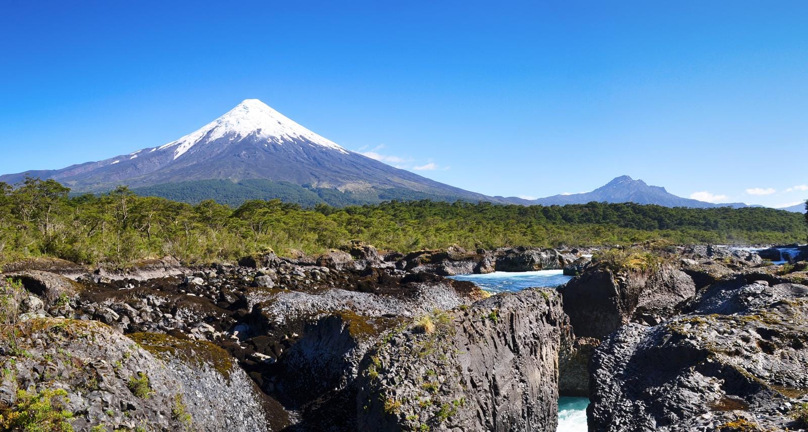 Schneebedeckter Vulkan Osorno in Chile, umgeben von grünen Wäldern und blauen Flüssen.