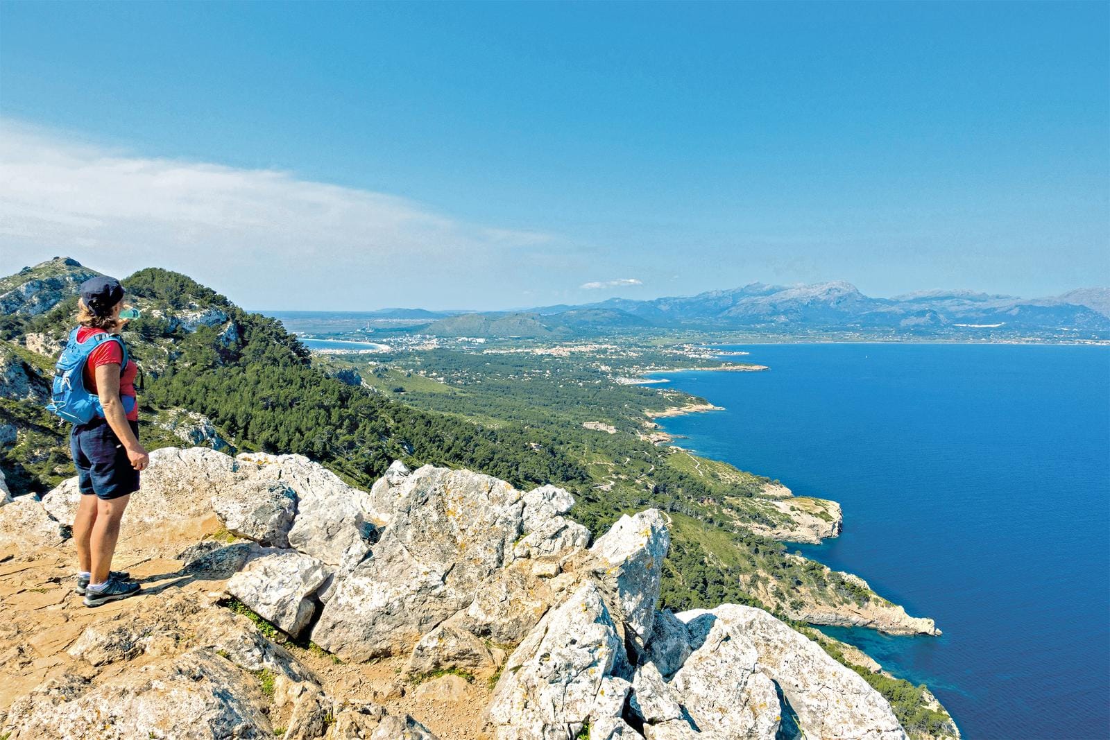 Eine Person genießt den Ausblick auf die Küste Mallorcas von einem felsigen Aussichtspunkt.