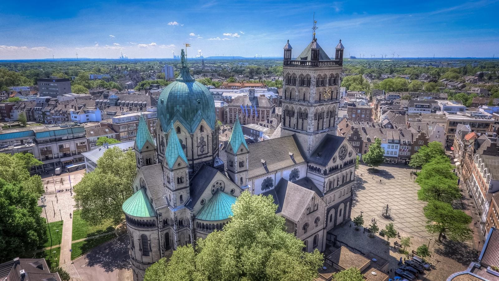 Romanische Kirche mit grünen Dächern in einer deutschen Stadt bei klarem Himmel.