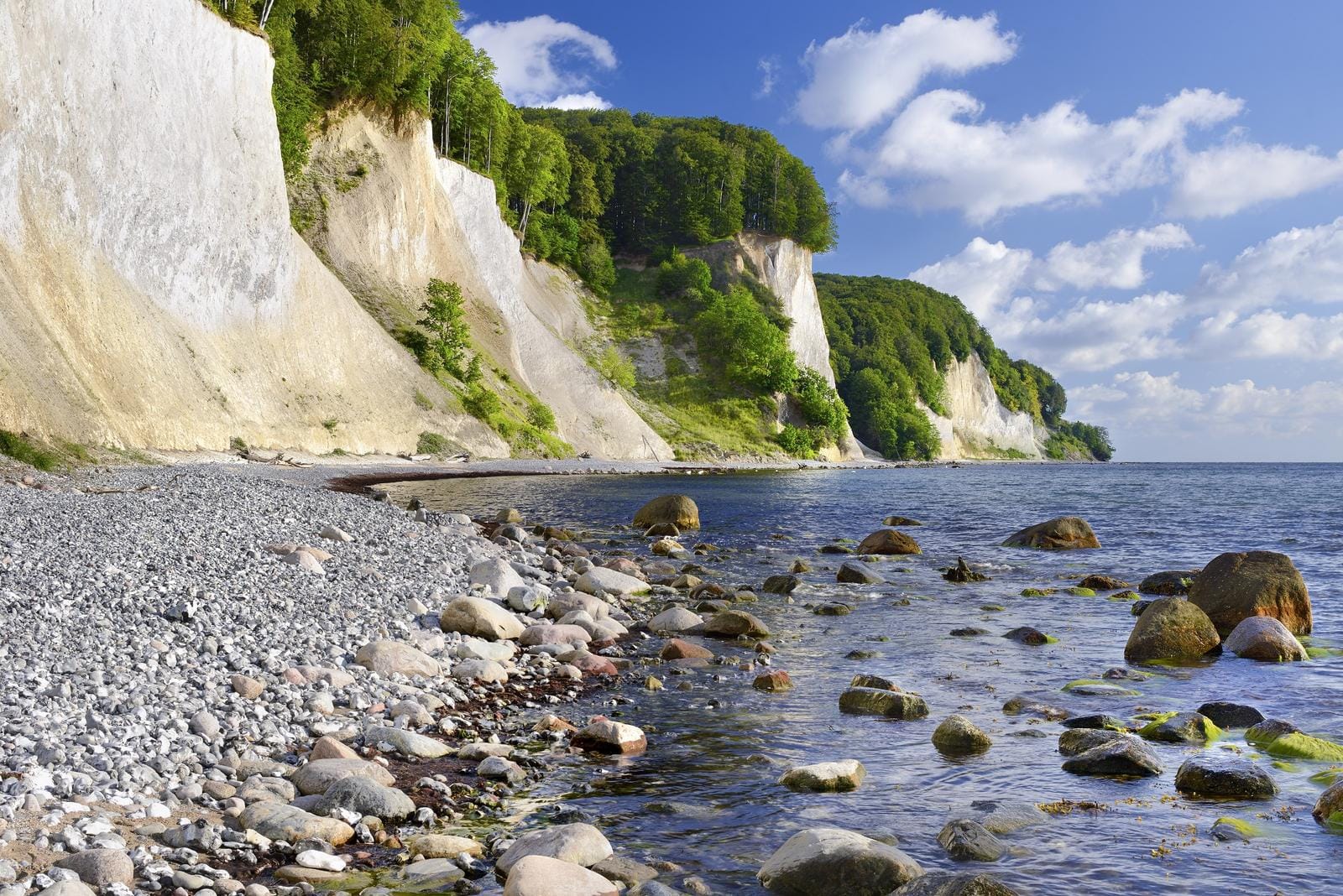Kreidefelsen auf Rügen, Deutschland, mit Kiesstrand und blauem Himmel.