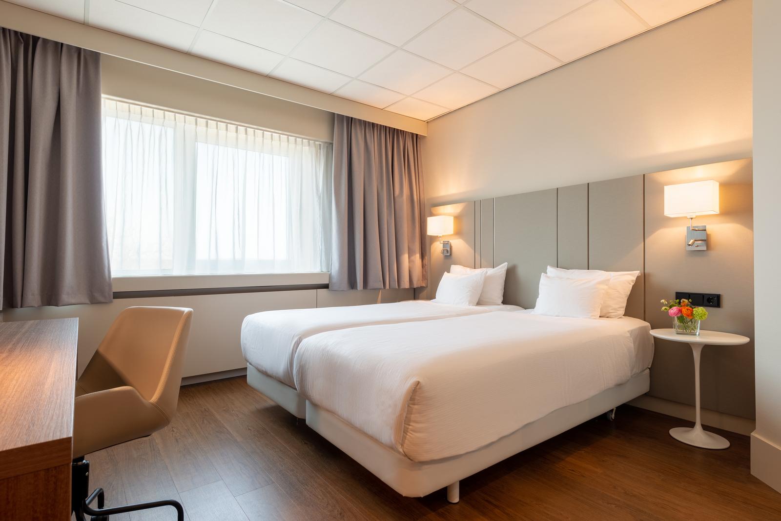 Modernes Hotelzimmer mit zwei Einzelbetten, Holzfußboden, helle Farben und Blumendekor.