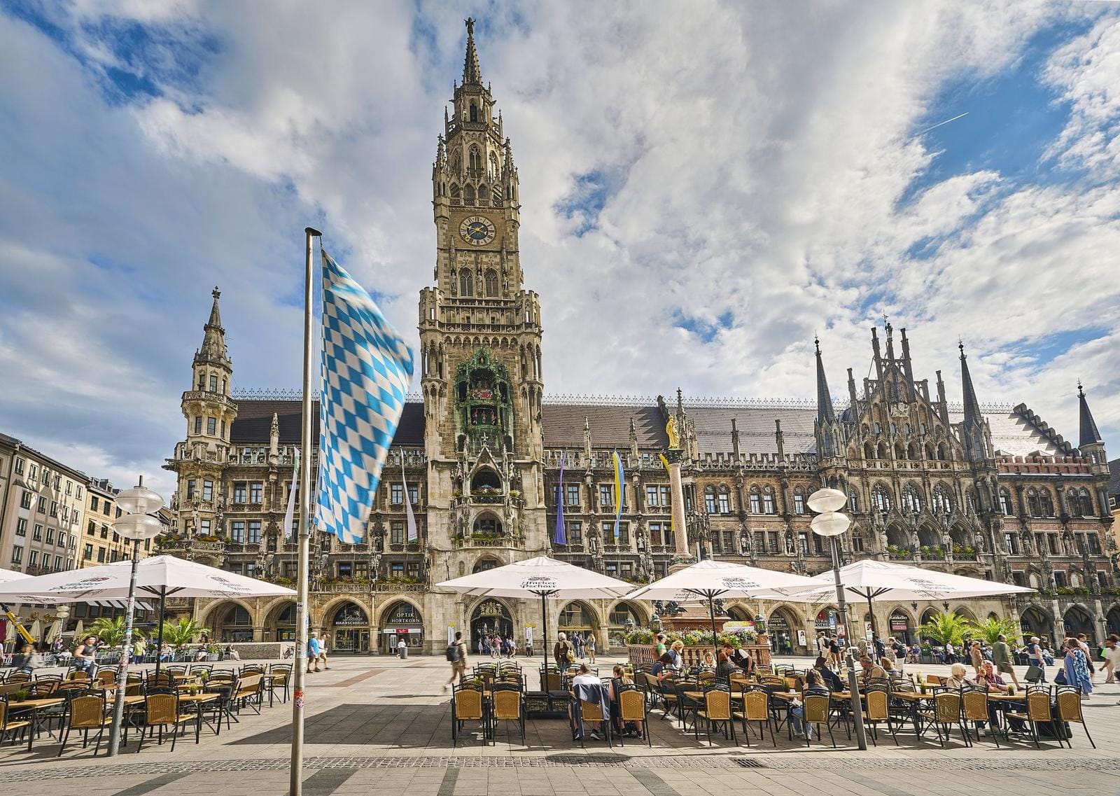 Rathaus München am Marienplatz mit bayerischer Flagge und Café-Terrasse.