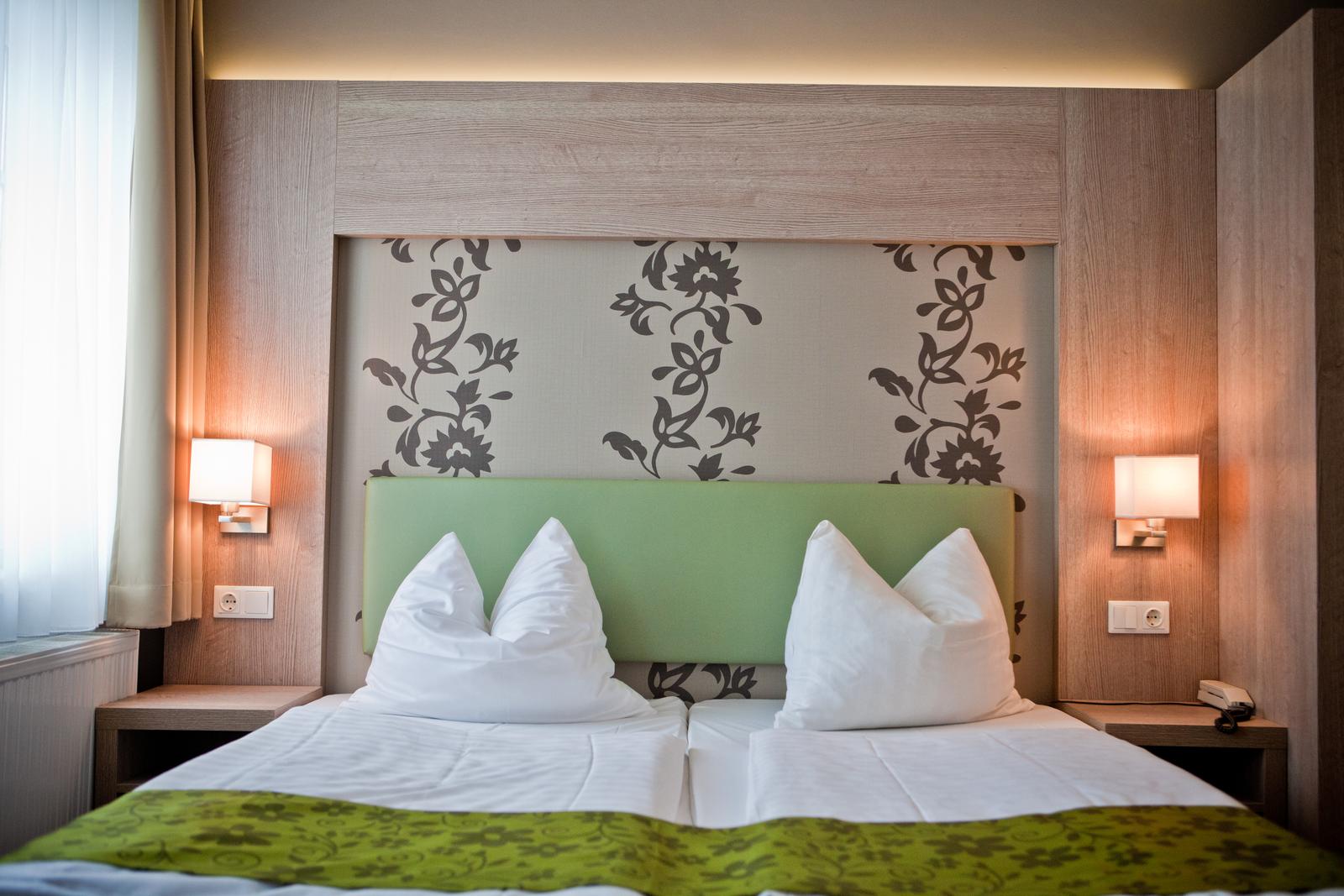 Modernes Hotelzimmer mit floraler Tapete und grünem Kopfteil, helles Ambiente.