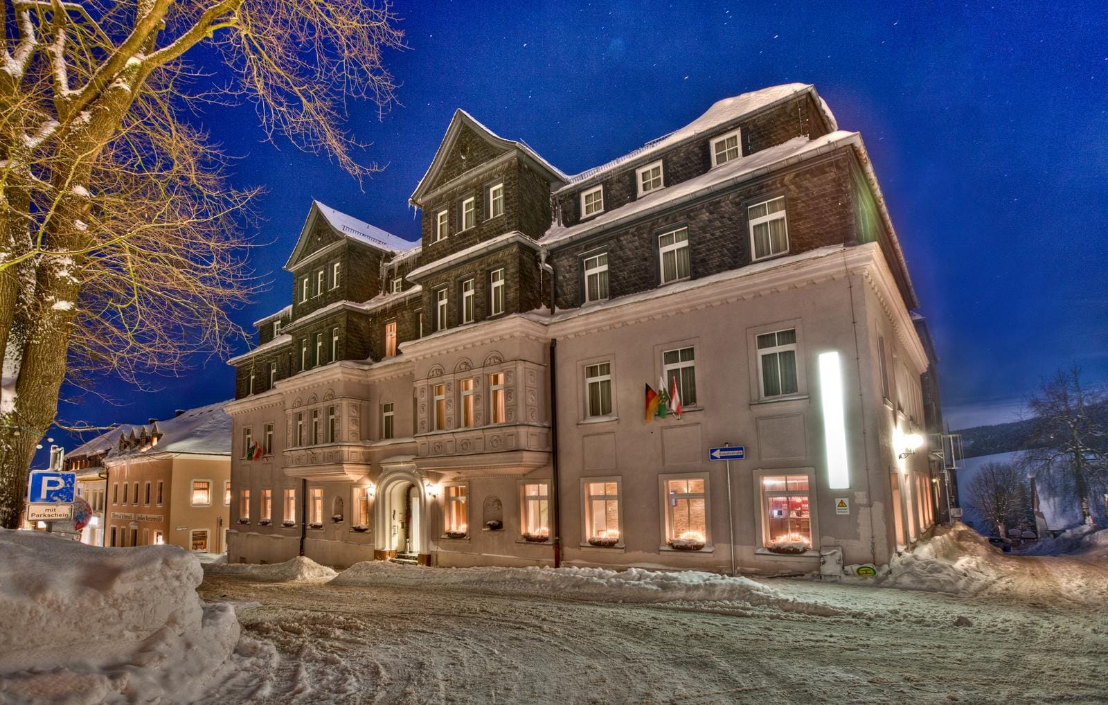 Historisches Hotel im Winter, beleuchtet, verschneite Umgebung, klare Nacht.