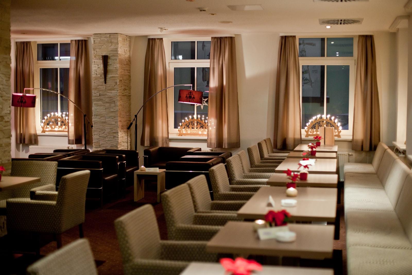 Gemütliche Hotel-Lobby mit braunen Sesseln, beige Vorhängen und stimmungsvoller Beleuchtung.