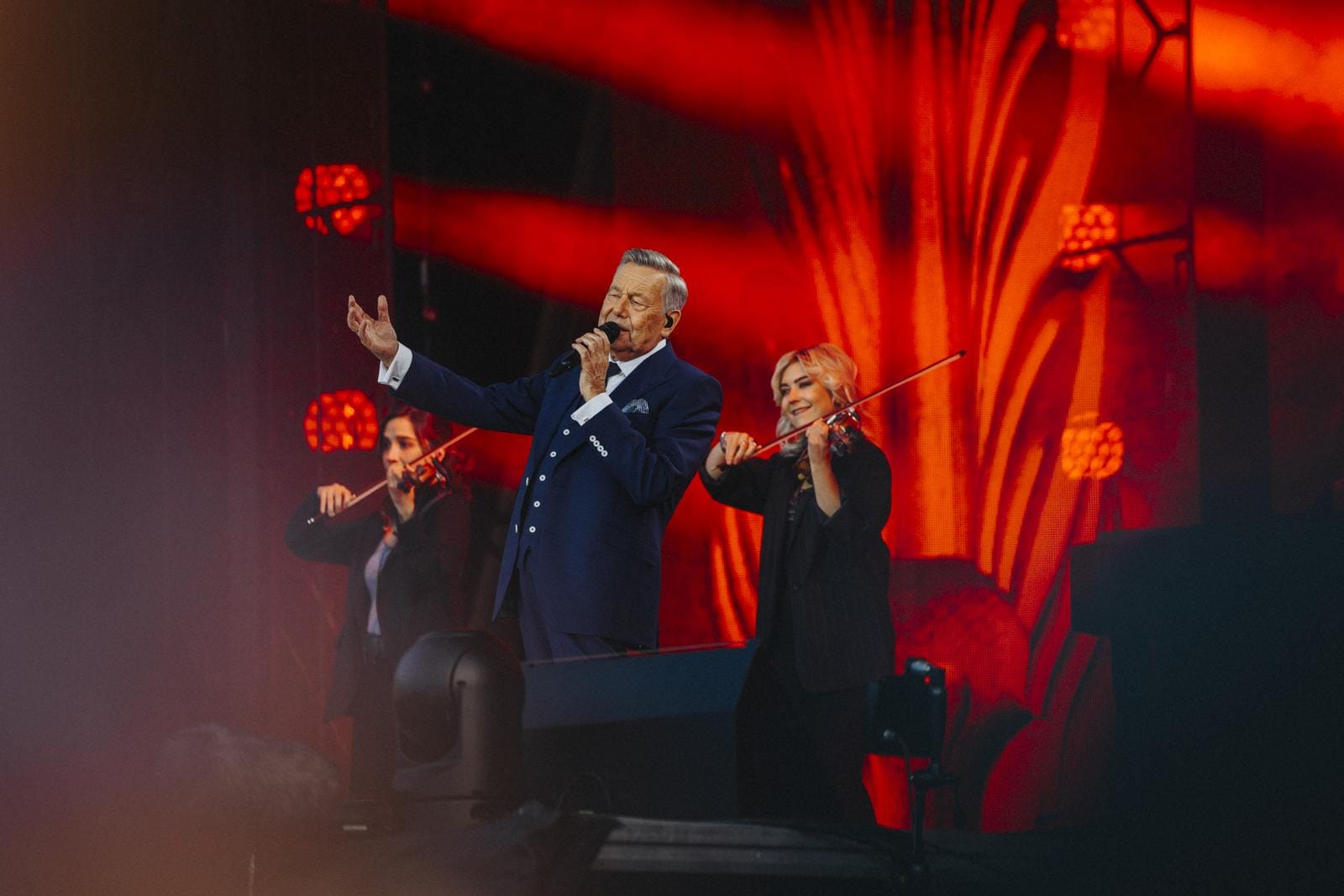 Konzertauftritt mit Sänger und Violinisten vor roter Lichtkulisse.