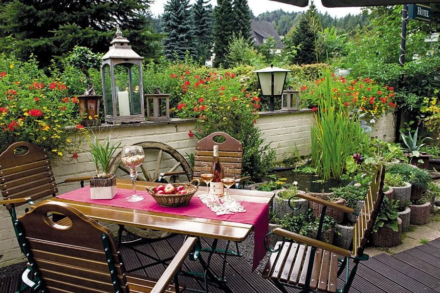 Gemütliche Terrasse mit Holzmöbeln, Blumen, Wein und stimmungsvollem Ambiente.