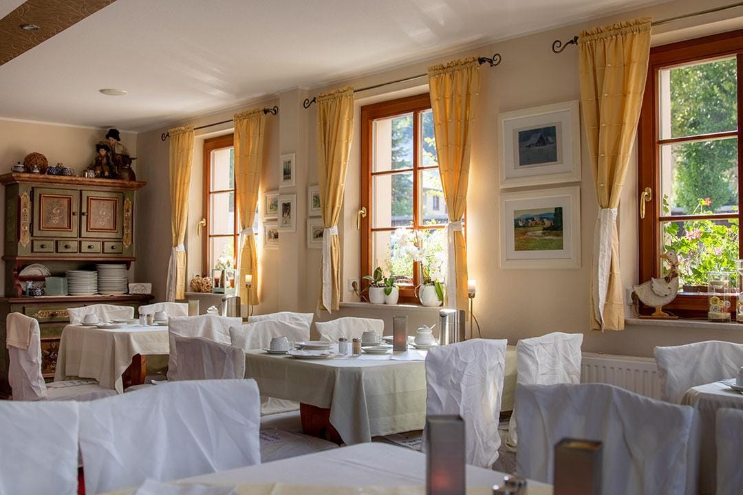 Gemütliches Hotel-Restaurant mit Sonnenschein, weißen Tischdecken und Bildern an der Wand.