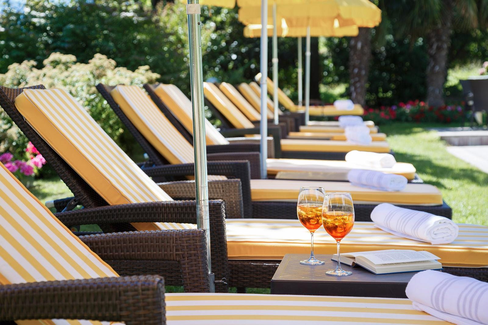 Gelbe gestreifte Liegen mit Sonnenschirmen, zwei Aperol-Spritz-Gläser auf Beistelltisch.