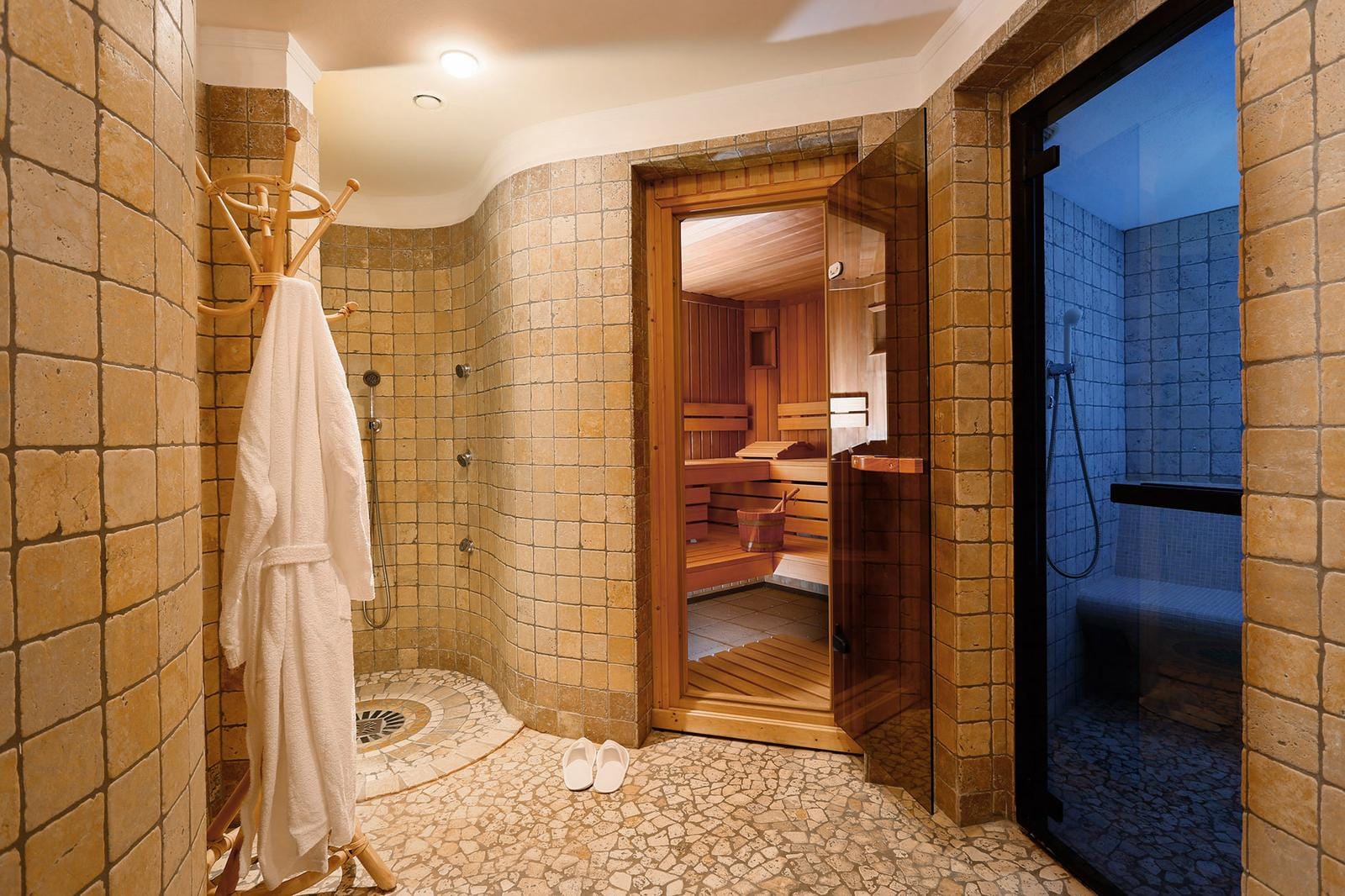 Wellnessbereich mit Sauna, Dusche, beigen Fliesen und Bademantel im gemütlichen Ambiente.