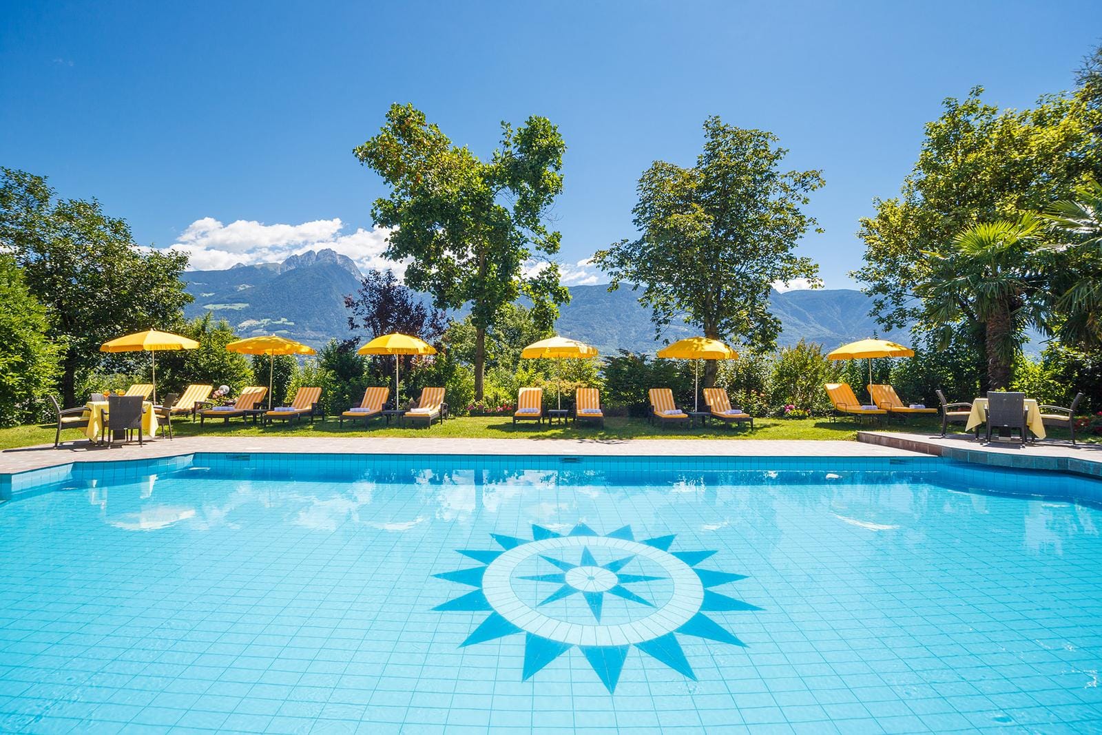 Strahlend blauer Pool mit gelben Liegen, Sonnenschirmen und Bergblick.