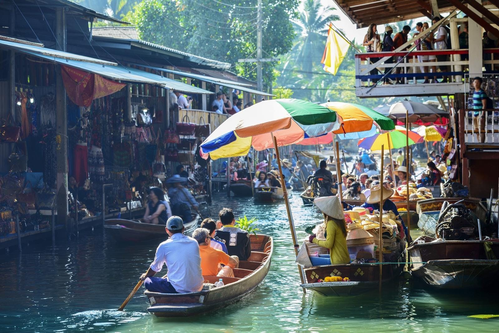 Schwimmender Markt in Thailand, Boote mit bunten Schirmen, viele Händler und Besucher.