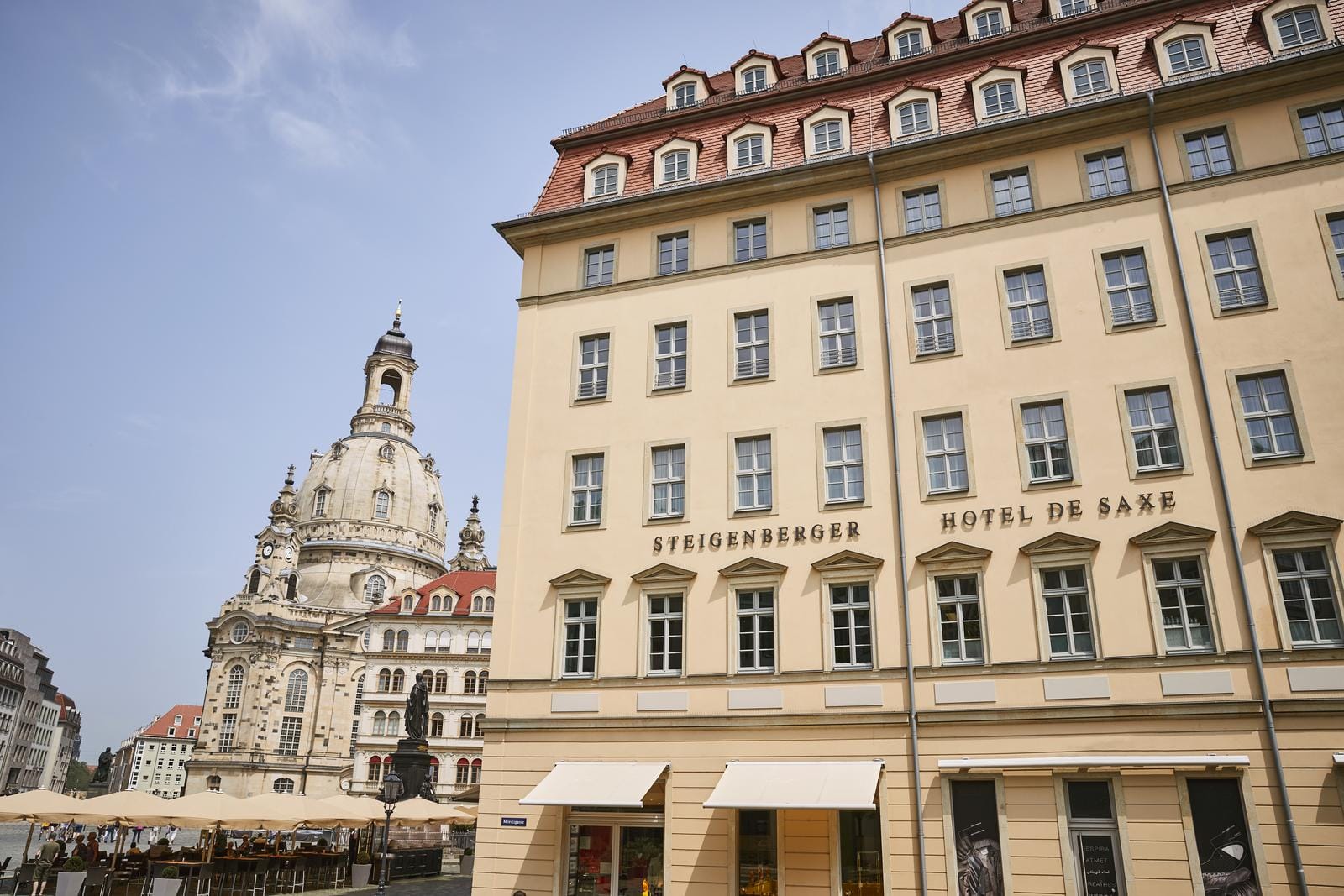 Hotel de Saxe in Dresden mit Frauenkirche und sonnigem Himmel im Hintergrund.