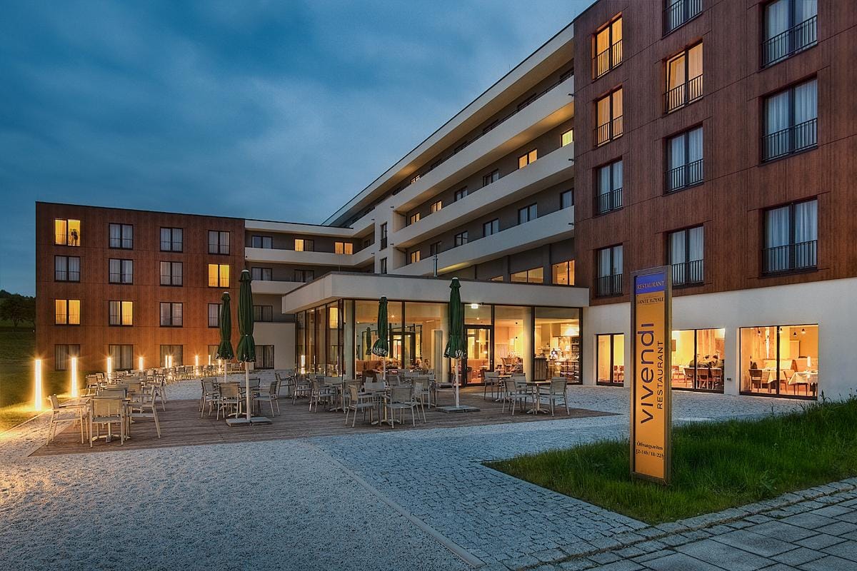 Modernes Hotel mit Holzelementen, beleuchteter Terrasse und Restaurant in Abenddämmerung.