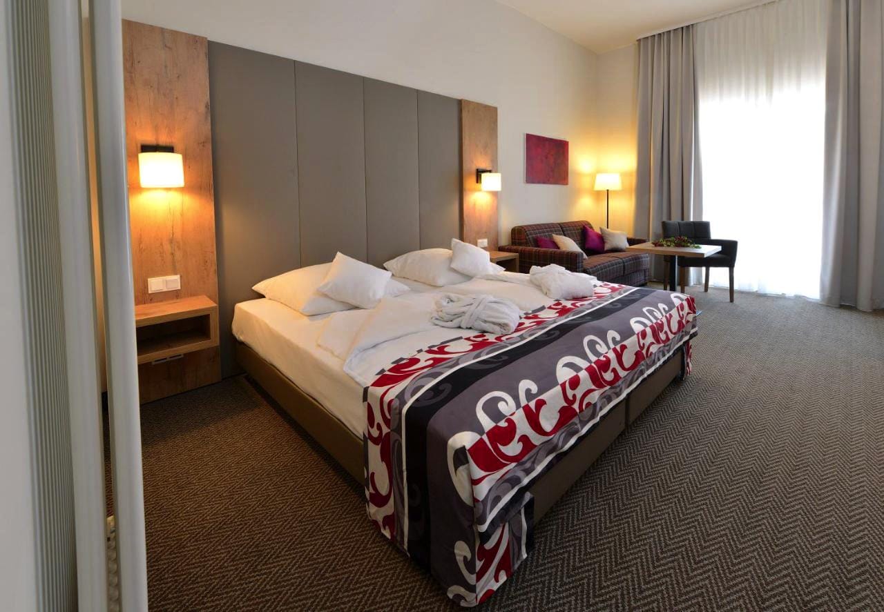 Modernes Hotelzimmer mit Doppelbett, Sofa und stilvoller Beleuchtung, in gemütlichen Erdtönen.