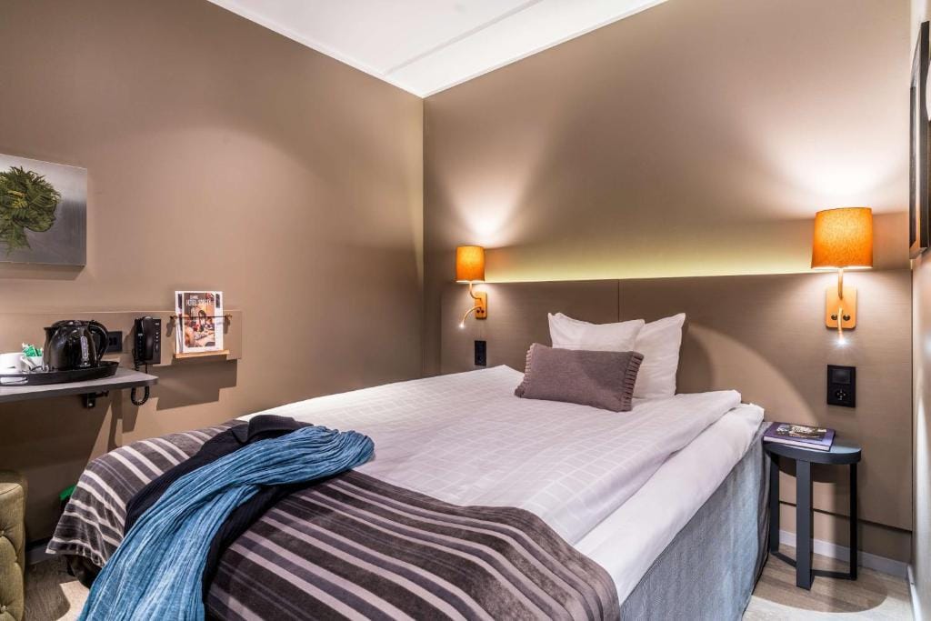 Modernes Hotelzimmer mit Doppelbett, warmen Lichtern und Wasserkocher, beige Wände.