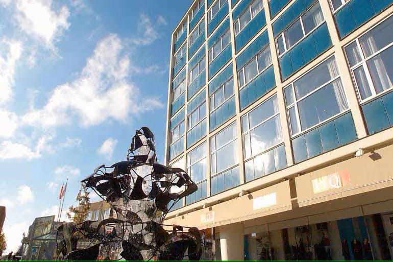 Moderner Fassadenbau mit Glasfenstern, blauem Himmel und abstrakter Skulptur im Vordergrund.