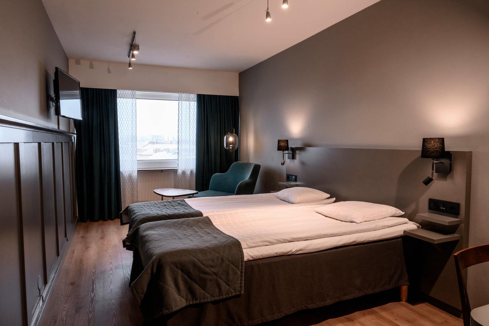 Modernes Hotelzimmer mit Doppelbett, grauen Wänden, Holzfußboden und gemütlichem Sessel.