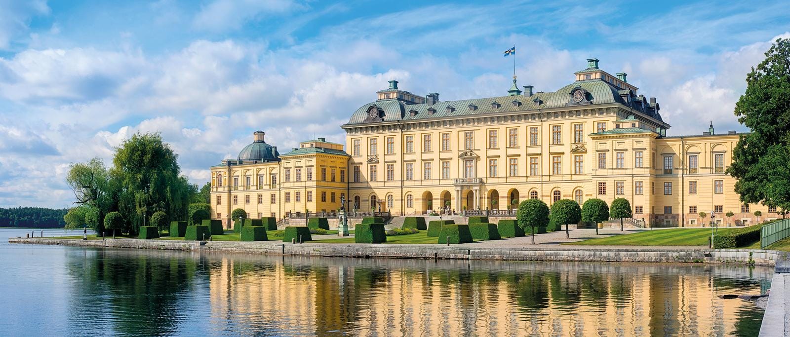 Gelbes Barockschloss Drottningholm, Schweden, am Wasser, umgeben von gepflegten Gärten.