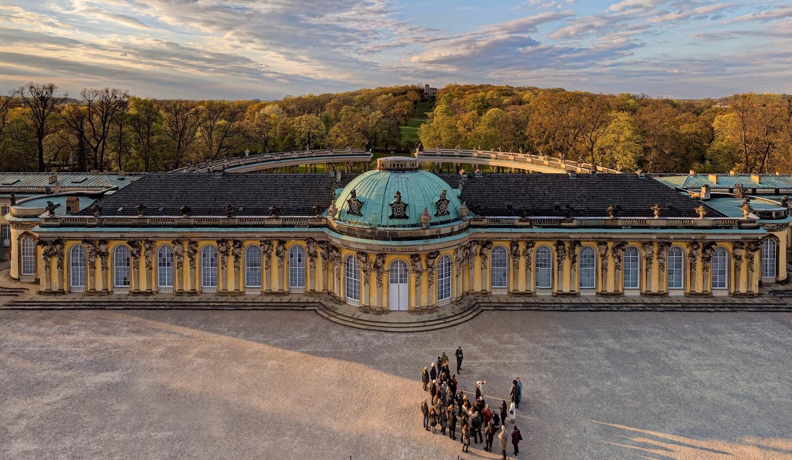 Barockschloss mit türkisfarbener Kuppel, umgeben von Bäumen im Herbstlicht.