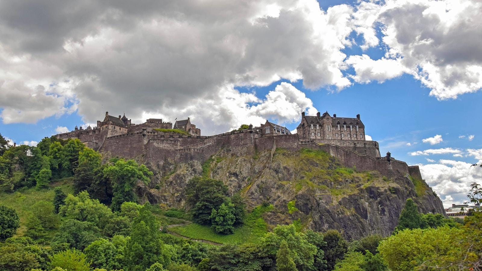 Schottland, Edinburgh, prächtige Burg auf grünem Hügel unter dramatischem Himmel.