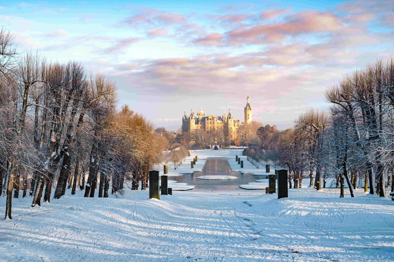 Winterliche Schlossansicht, verschneite Allee, Schloss am Ende, pastellfarbener Himmel.